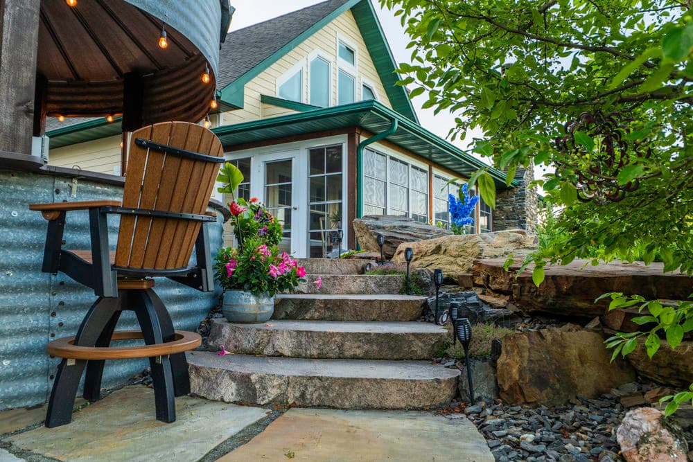 Charming outdoor seating area with stone steps, lush plants, and modern house facade.