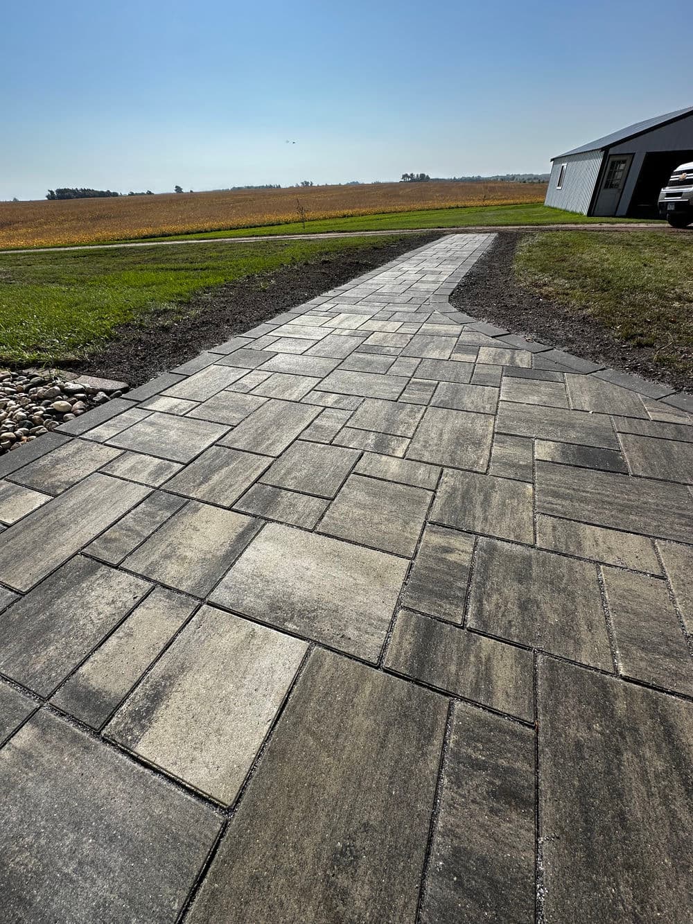 Paved pathway leading to a building with a clear blue sky and agricultural fields.