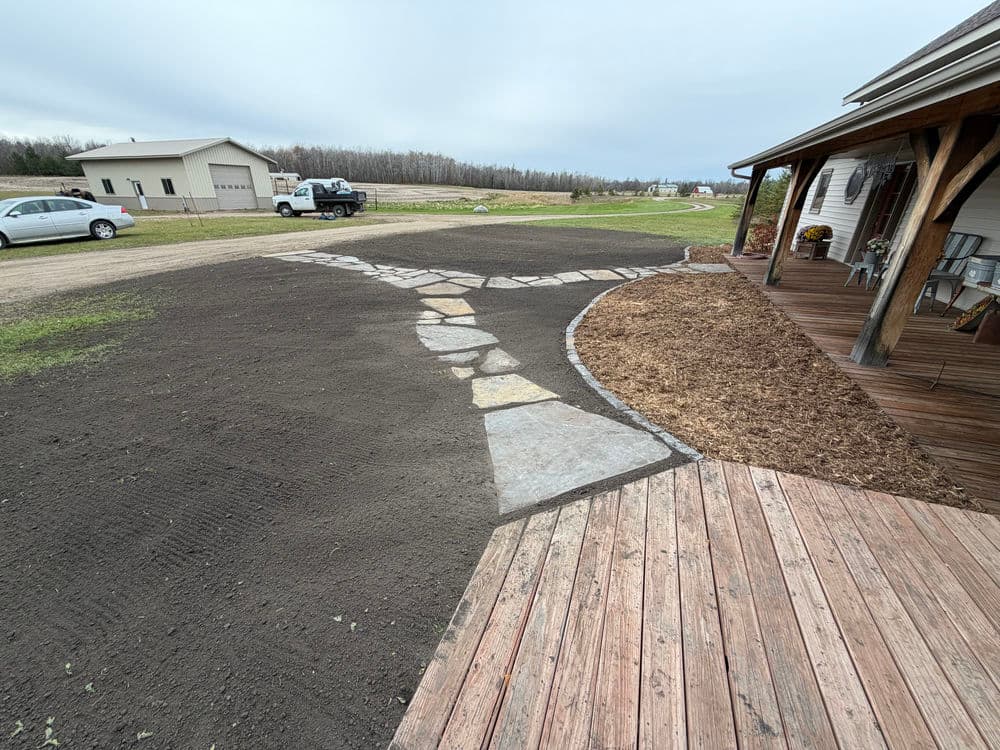Residential landscape design featuring a stone pathway, fresh mulch, and vehicles parked nearby.
