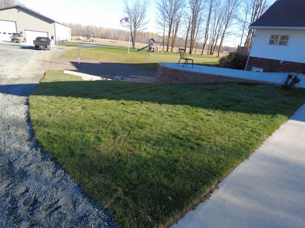 Lush green lawn with gravel driveway, playground in background, and trees lining the property.