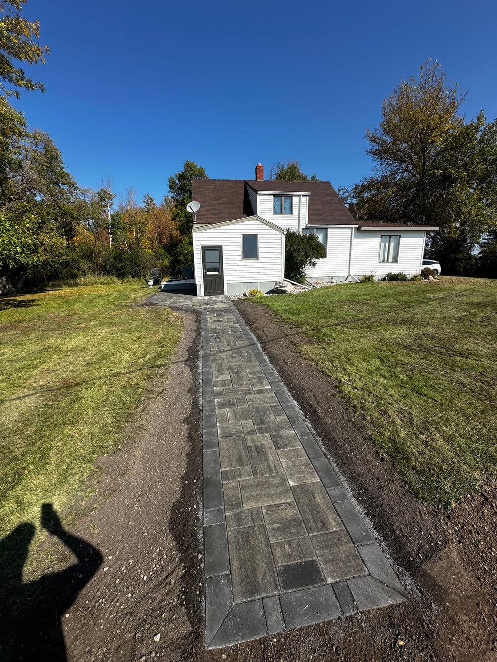 Newly paved stone walkway leading to a white house surrounded by greenery and blue sky.