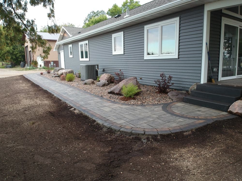 Paved walkway alongside modern home, featuring decorative rocks and landscaping elements.