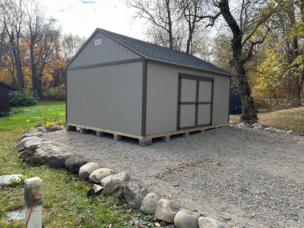 Storage shed on a gravel base, surrounded by rocks and autumn foliage.