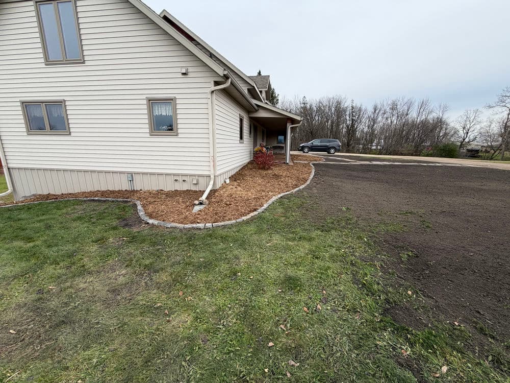 Side view of a home with landscaped garden, mulch beds, and freshly cleared dirt area.